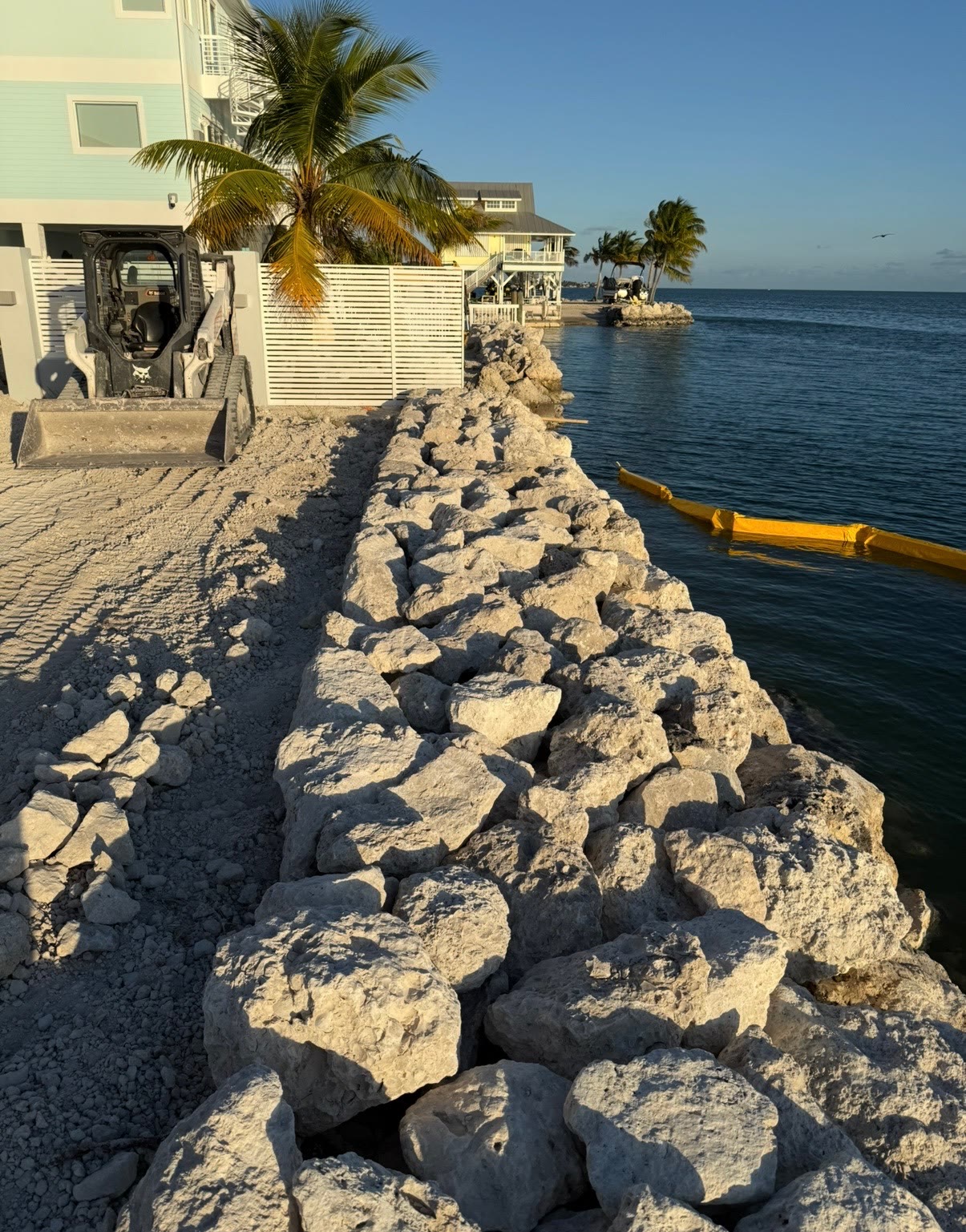 Rip-rap coral rock retaining wall installation with Bobcat skid-steer on a Florida Keys oceanfront property — Alex Landscaping seawall build.